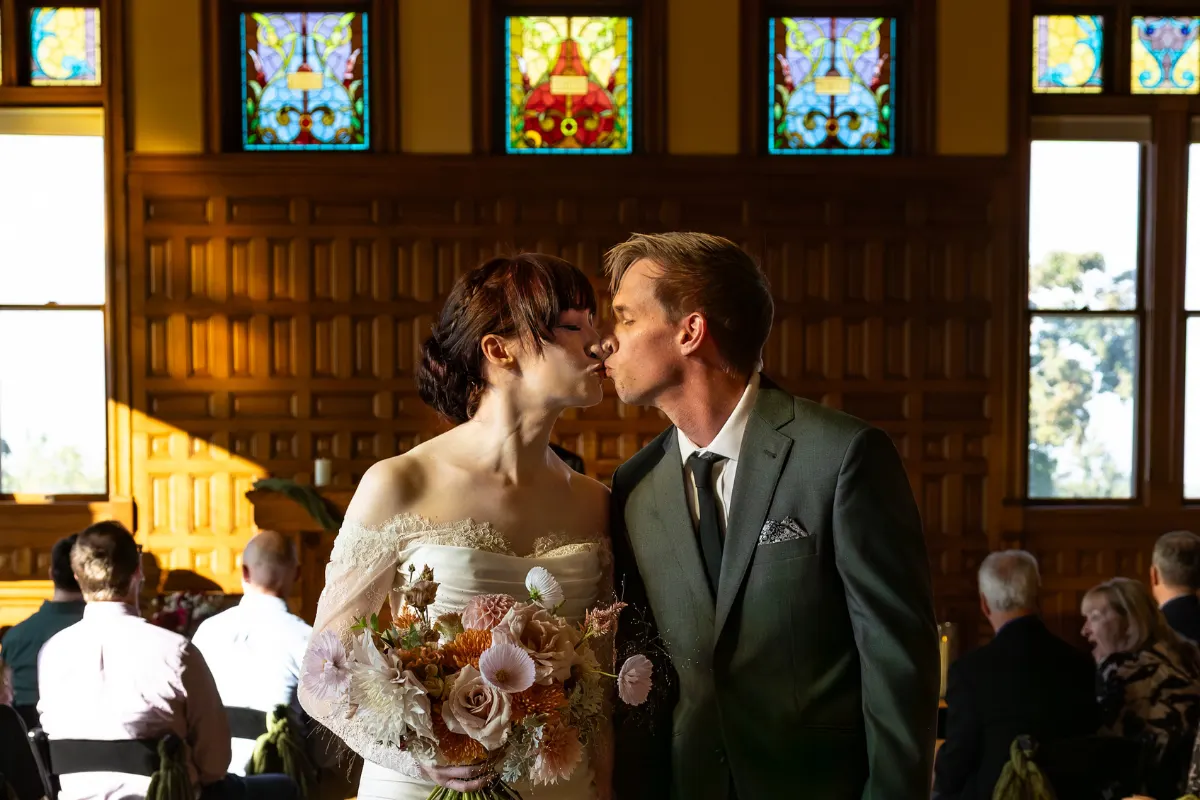 Bride and groom sharing a kiss with bridal bouquet visible